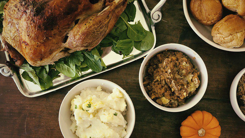 Thanksgiving meal: turkey, mashed potatoes, stuffing, and bread rolls on wooden table