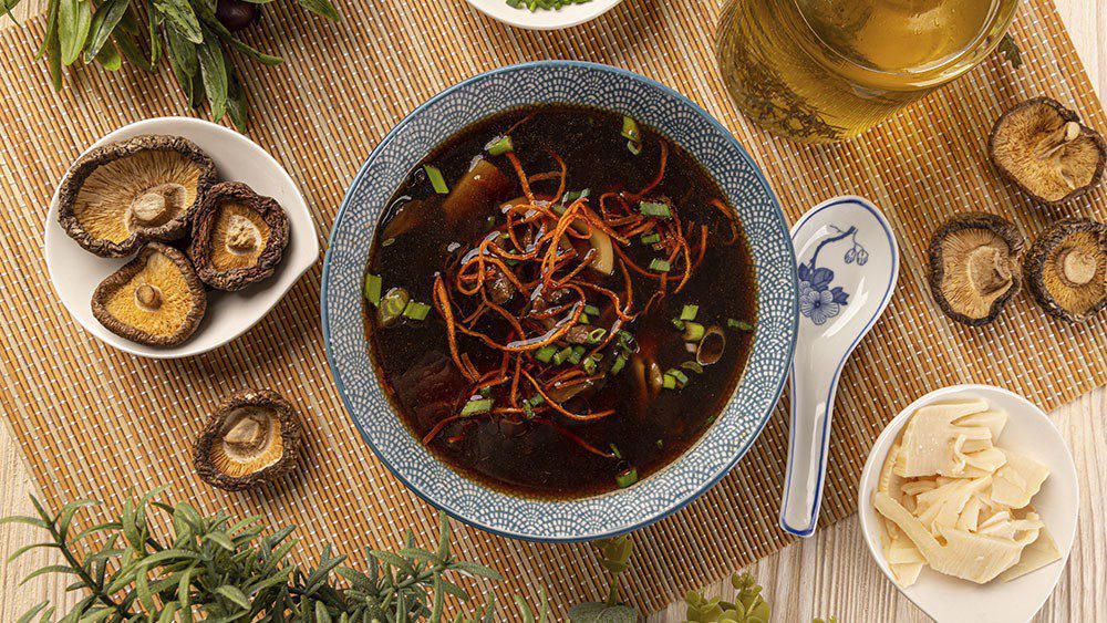 Medicinal soup and dried mushrooms on the side. Soup has dark broth with scallions and thinly sliced carrots floating on the top.