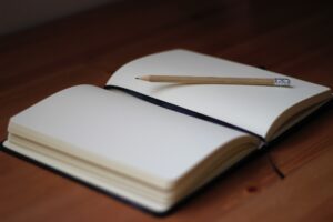 Open notebook with blank pages. Pencil is resting diagonally across right page