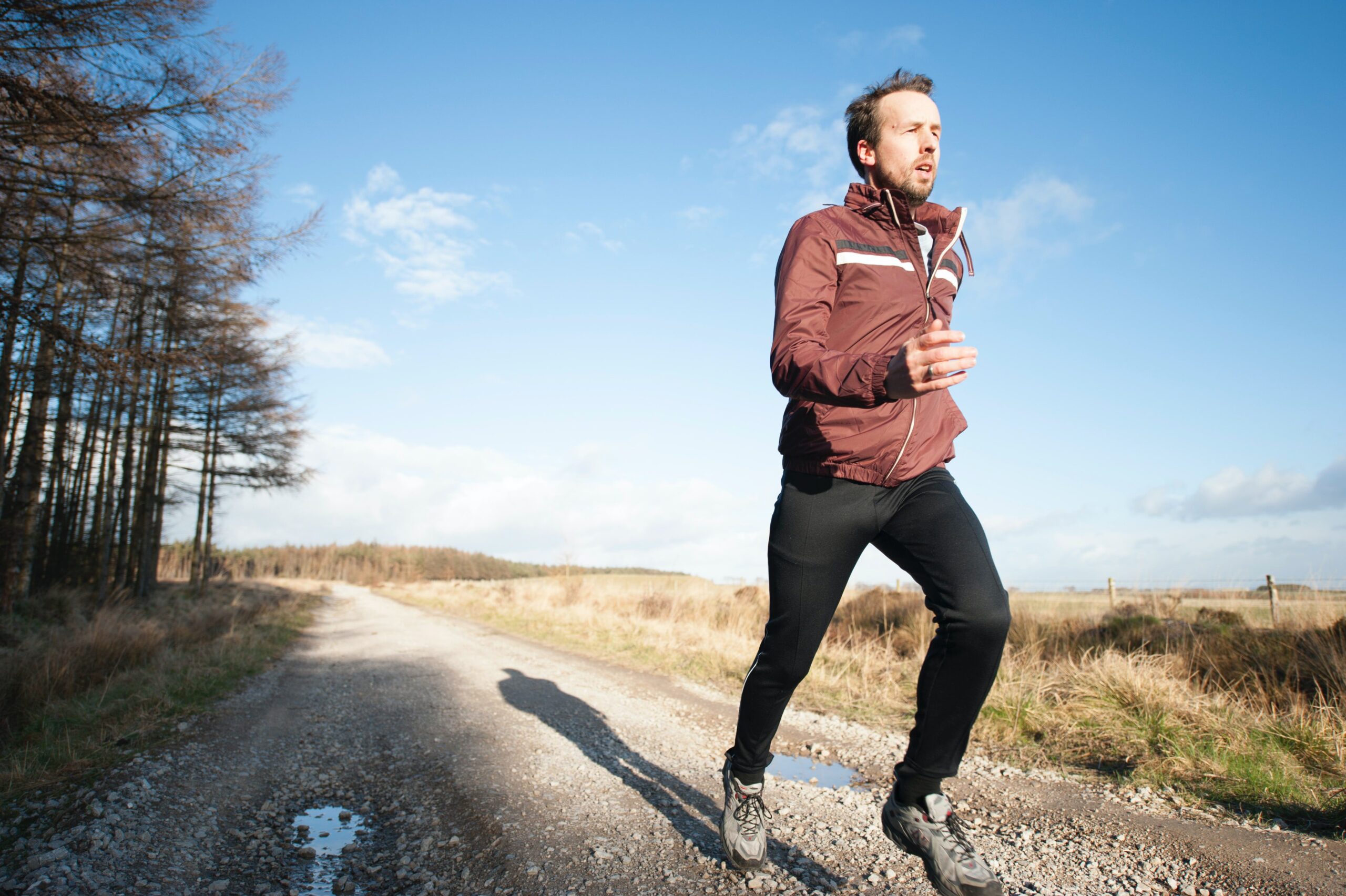 Person running outside on trail between the woods and a field