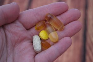 Vitamins and supplements in palm of hand. 4 orange gel capsules and 2 tablets. 