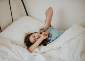 Person sleeping in bed with white sheets. Stretching their hands above their head