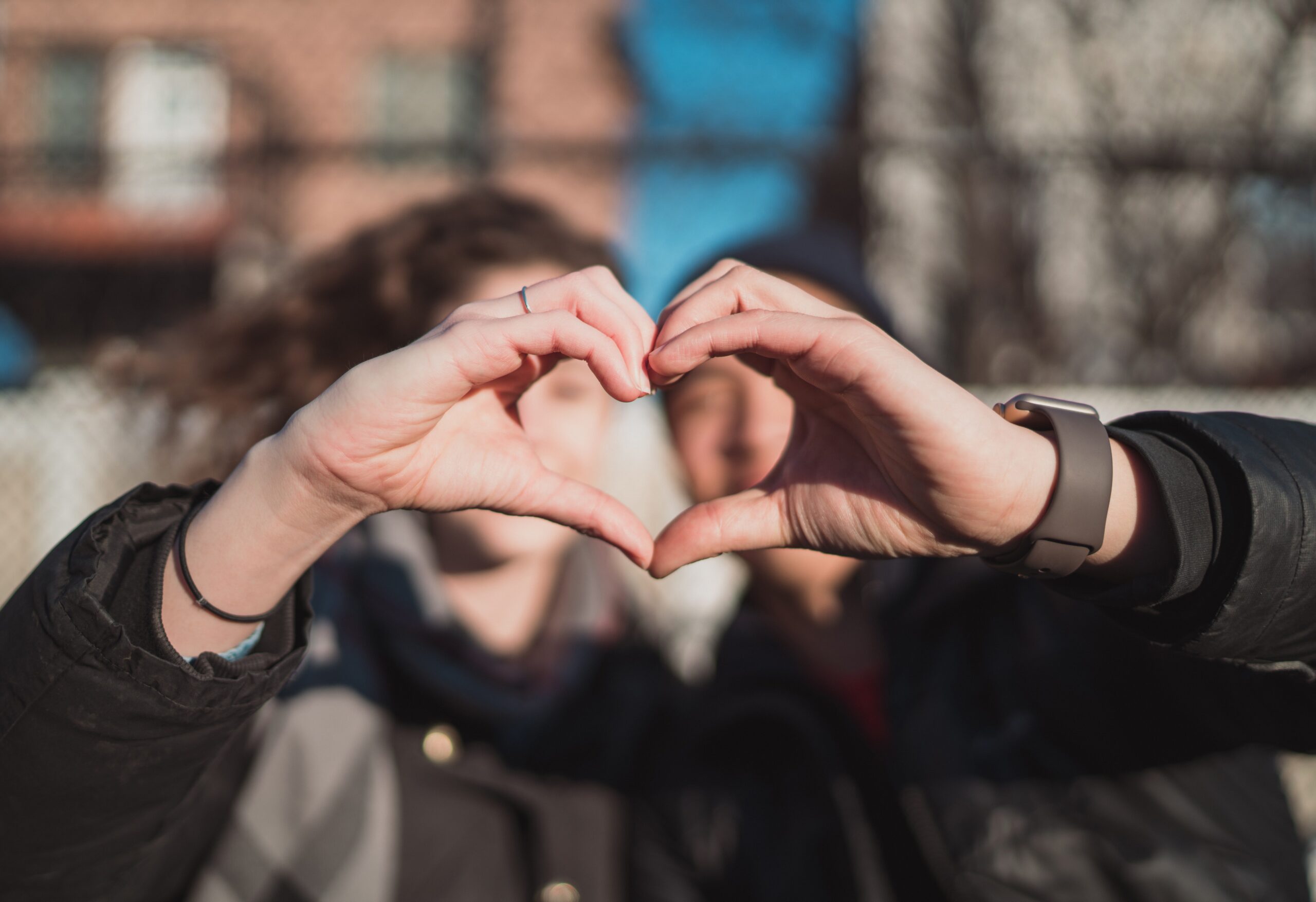 2 people, each holding out one curved hand to create a heart together.