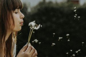 Person blowing on dandelion flower