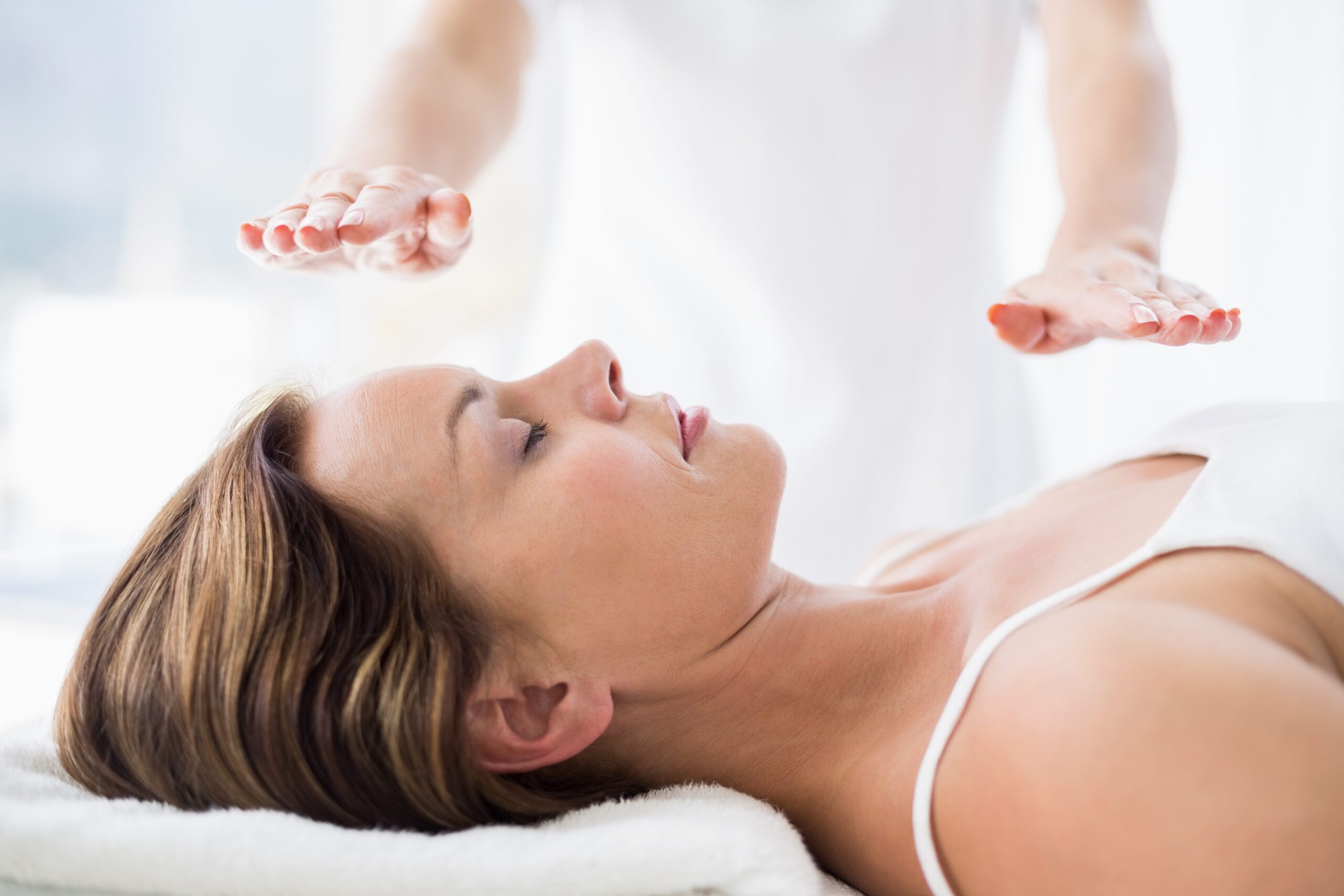 Reiki treatment. Patient laying face up with eyes closed while practitioner holding hands a few inches above them