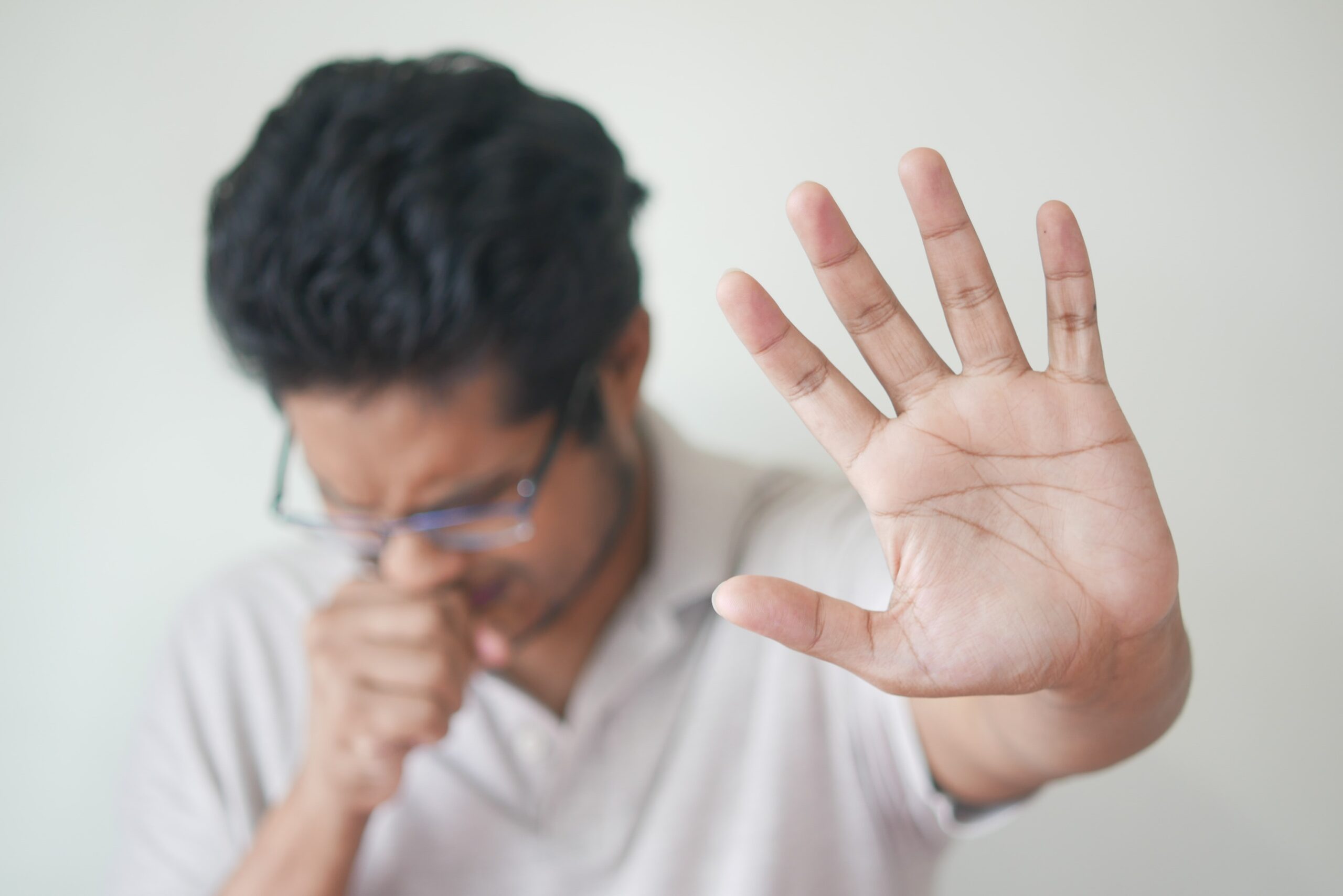 Person covering cough and holding hand out to stop someone from coming near them